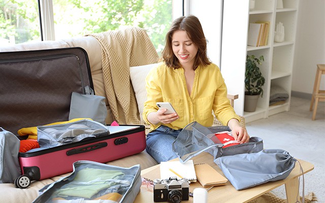 Eine Frau sitzt auf der Couch und packt ihren Koffer mit Kleidung.
