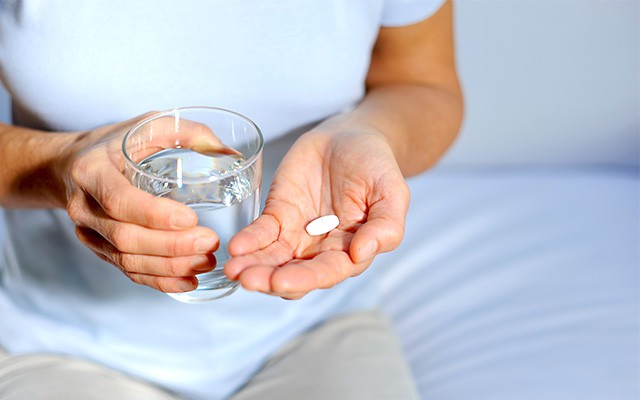 Eine Person hält ein Glas Wasser und eine Tablette in der Hand.