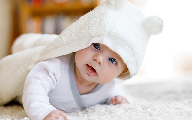 Ein Baby liegt unter einer weißen Decke mit Bärenohren auf dem Boden.