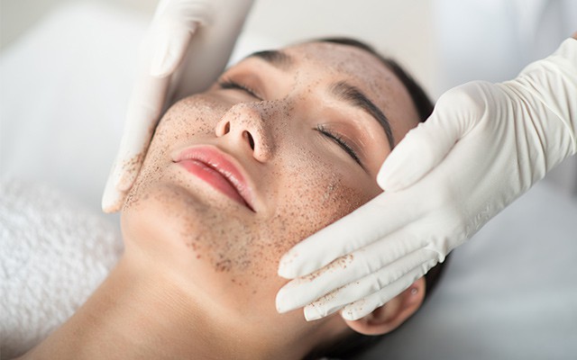 Eine Person erhält eine Gesichtsbehandlung mit Peeling und geschlossenen Augen.