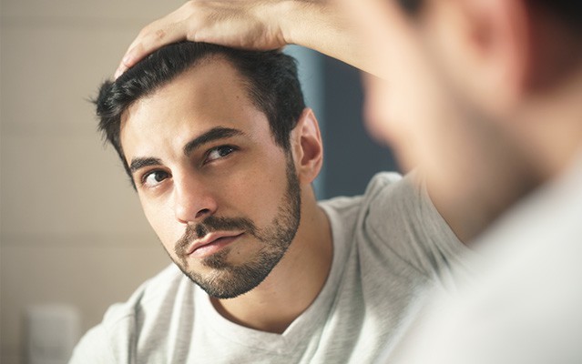 Ein Mann betrachtet sein Haar nachdenklich im Spiegel.