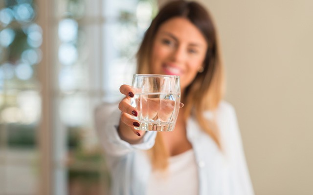 Eine Frau hält ein Glas Wasser in die Kamera.