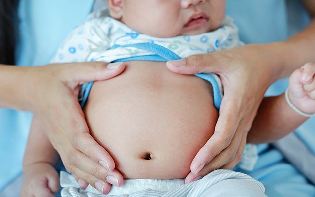 Eine Person hält den Bauch eines Babys mit ihren Händen.