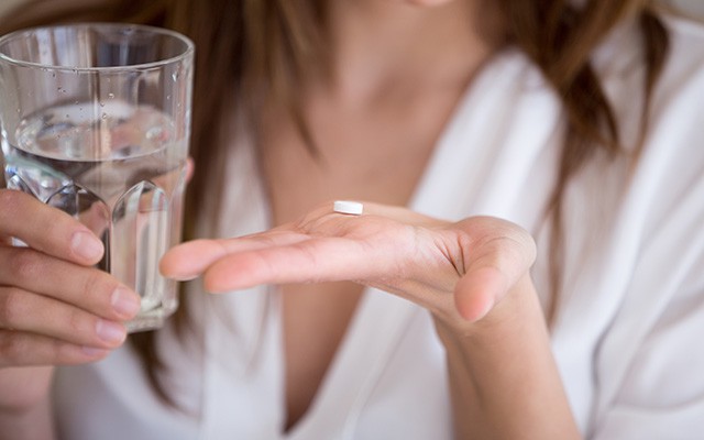 Eine Person hält ein Glas Wasser und eine weiße Tablette in der Hand.
