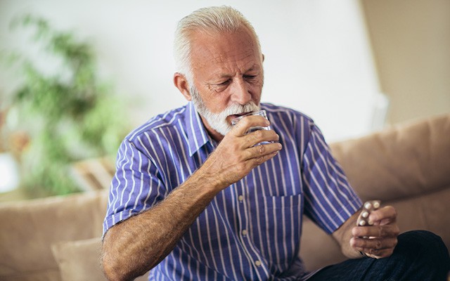 Älterer Mann trinkt Wasser und hält Tabletten in der Hand.