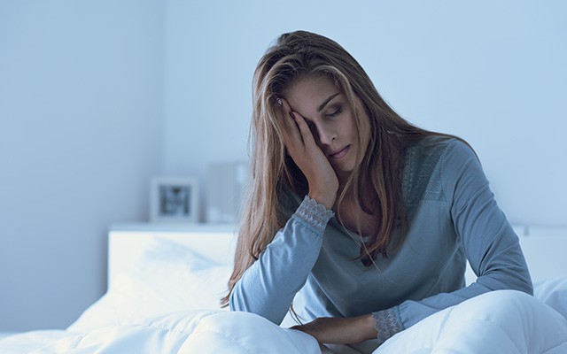 Eine Frau sitzt im Bett und hält sich müde den Kopf.