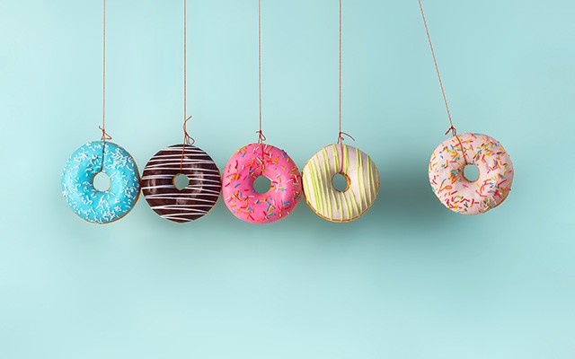 F&uuml;nf bunte Donuts h&auml;ngen an roten Schn&uuml;ren vor einem hellblauen Hintergrund.