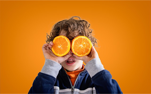 Ein Kind hält zwei Orangenscheiben vor seine Augen.