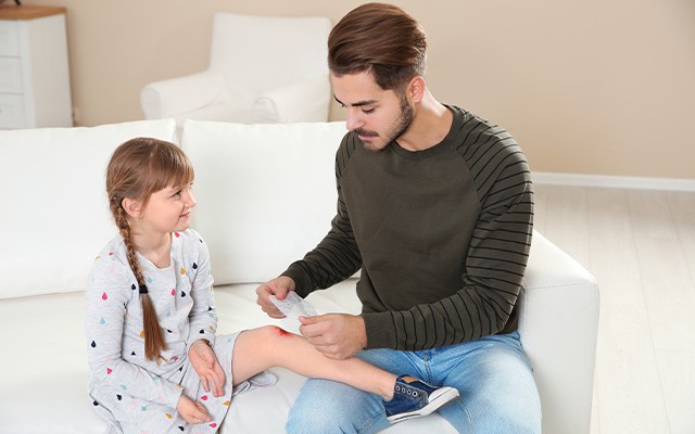 Ein Mann verarztet das Knie eines Mädchens.