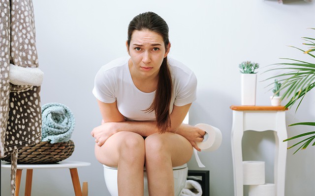 Eine Frau sitzt auf der Toilette und hält Toilettenpapier.