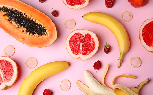 Bananen, Grapefruit, Papaya und Erdbeeren liegen dekorativ auf rosa Hintergrund verteilt.
