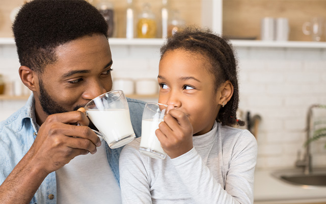 Ein Mann und ein Mädchen trinken in der Küche Milch aus Gläsern.