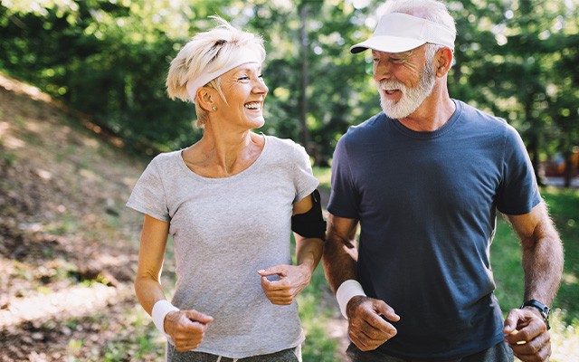 Zwei ältere Personen joggen glücklich im Wald.