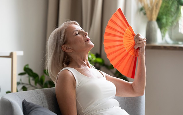 Frau fächert sich auf dem Sofa Luft zu mit einem orangefarbenen Fächer.