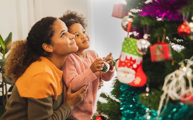 Eine Frau und ein Kind schmücken einen Weihnachtsbaum zusammen.