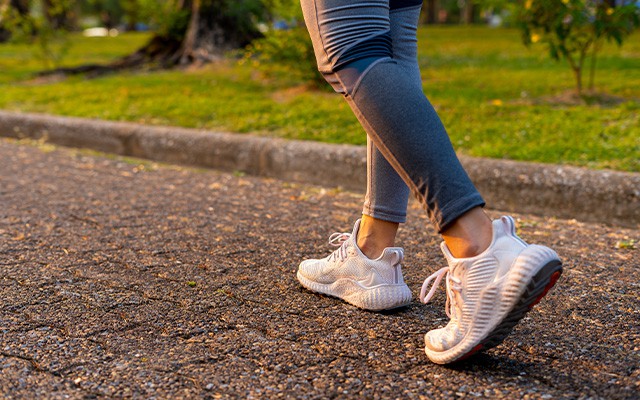 Eine Person geht in weißen Turnschuhen auf einem Gehweg im Park spazieren.