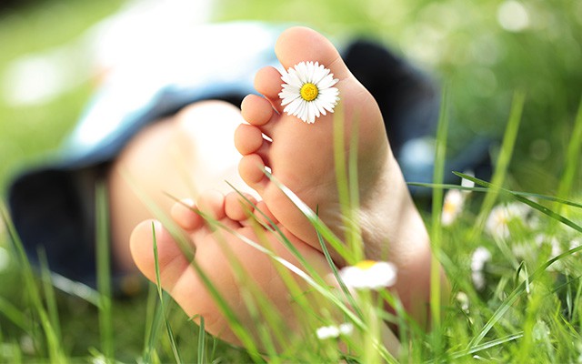 Barfuß im Gras mit Gänseblümchen zwischen den Zehen.