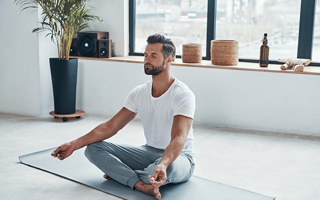 Ein Mann meditiert im Schneidersitz auf einer Yogamatte.