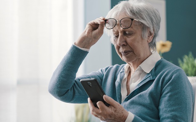 Ältere Frau betrachtet ein Smartphone und hebt ihre Brille an.