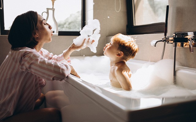 Eine Frau und ein Kind spielen mit Schaum in einer Badewanne.