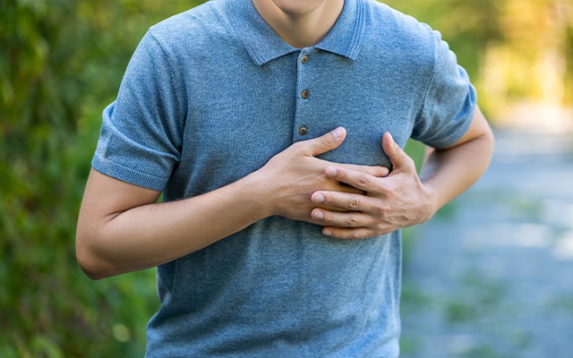 Eine Person in einem blauen Shirt hält sich die Brust.