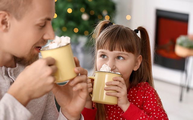 Kind und Erwachsener trinken heiße Schokolade mit Sahne aus gelben Tassen.