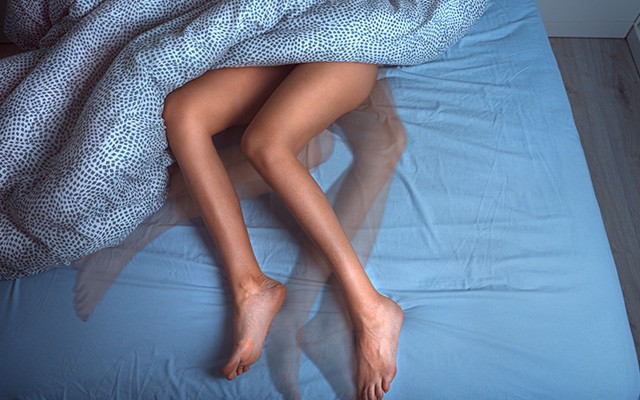 Eine Person liegt unter einer Decke auf einem blauen Bett.