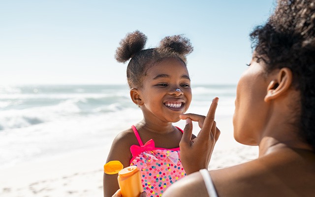 Ein Kind bekommt am Strand Sonnencreme aufgetragen.