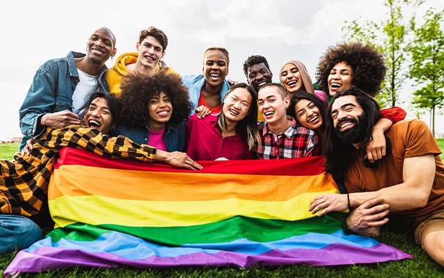 Eine fröhliche Gruppe hält eine bunte Regenbogenfahne im Freien.