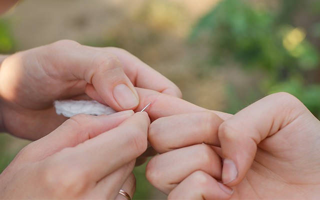 Zwei Hände entfernen vorsichtig einen Splitter aus einem Finger.