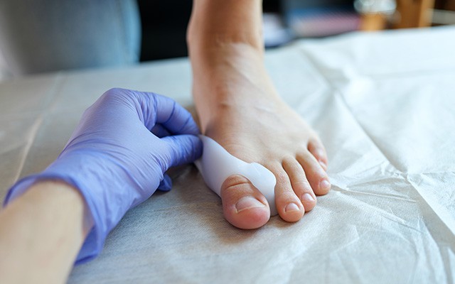 Eine Hand in einem lila Handschuh behandelt einen Fuß mit einer Bandage.