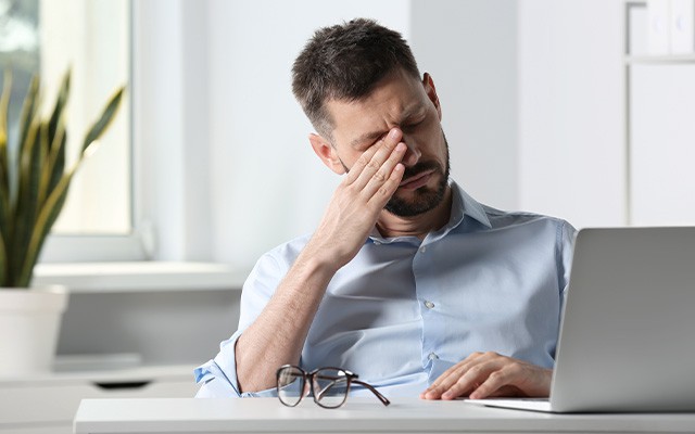 Ein Mann sitzt am Tisch und reibt sich müde die Augen.