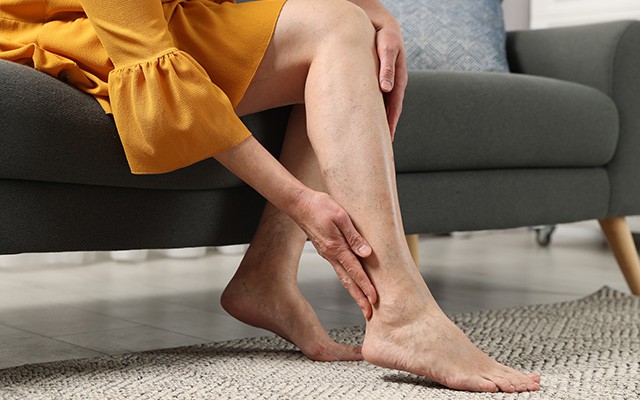 Eine Person sitzt auf einem Sofa und hält ihr Bein mit der Hand.