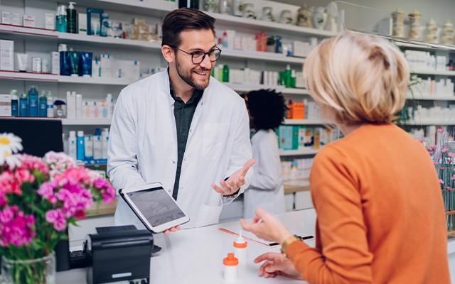 Ein Apotheker spricht lächelnd mit einer Kundin an der Theke.