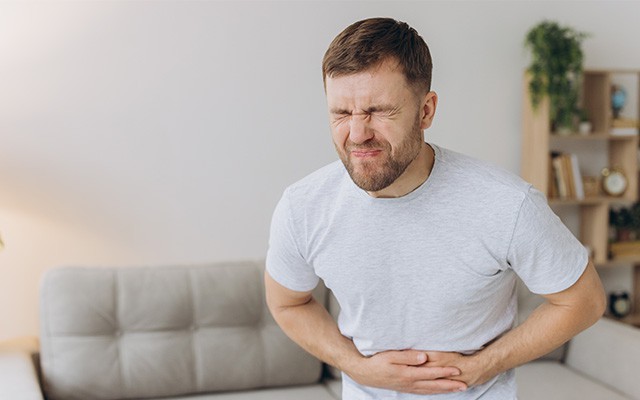 Ein Mann hält sich schmerzerfüllt den Bauch im Wohnzimmer.