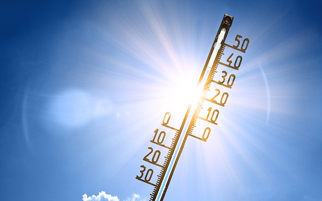 Thermometer zeigt hohe Temperaturen vor strahlender Sonne und blauem Himmel.